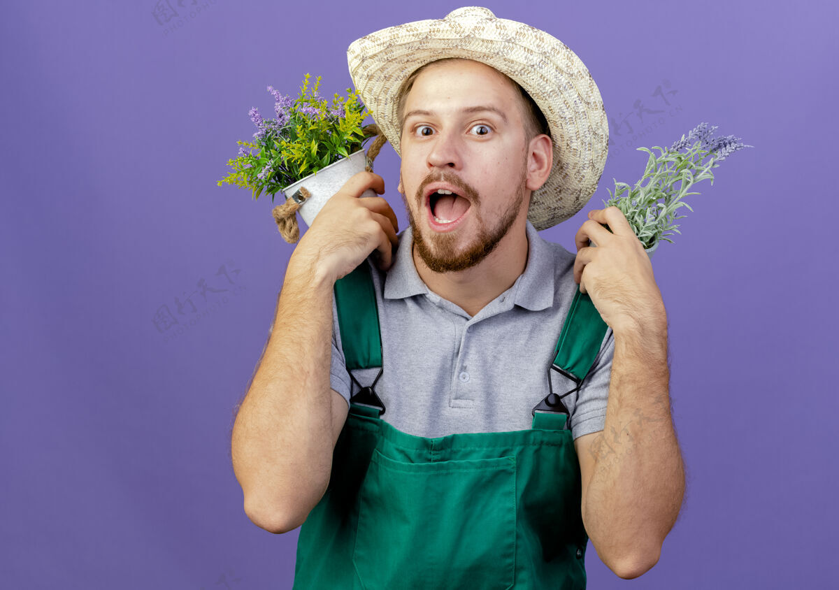 人印象深刻的年轻英俊的斯拉夫园丁在制服和帽子举行花盆在肩上看制服紫色帅气