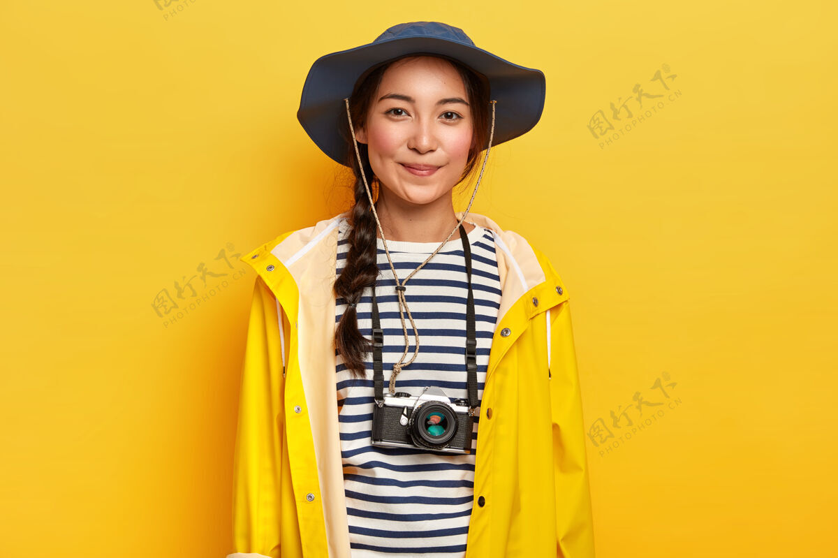 模特有才华的女摄影师在冒险之旅中进行专业拍摄 使用复古相机 戴时尚帽子 穿黄色雨衣 享受假期年轻人服装爱好