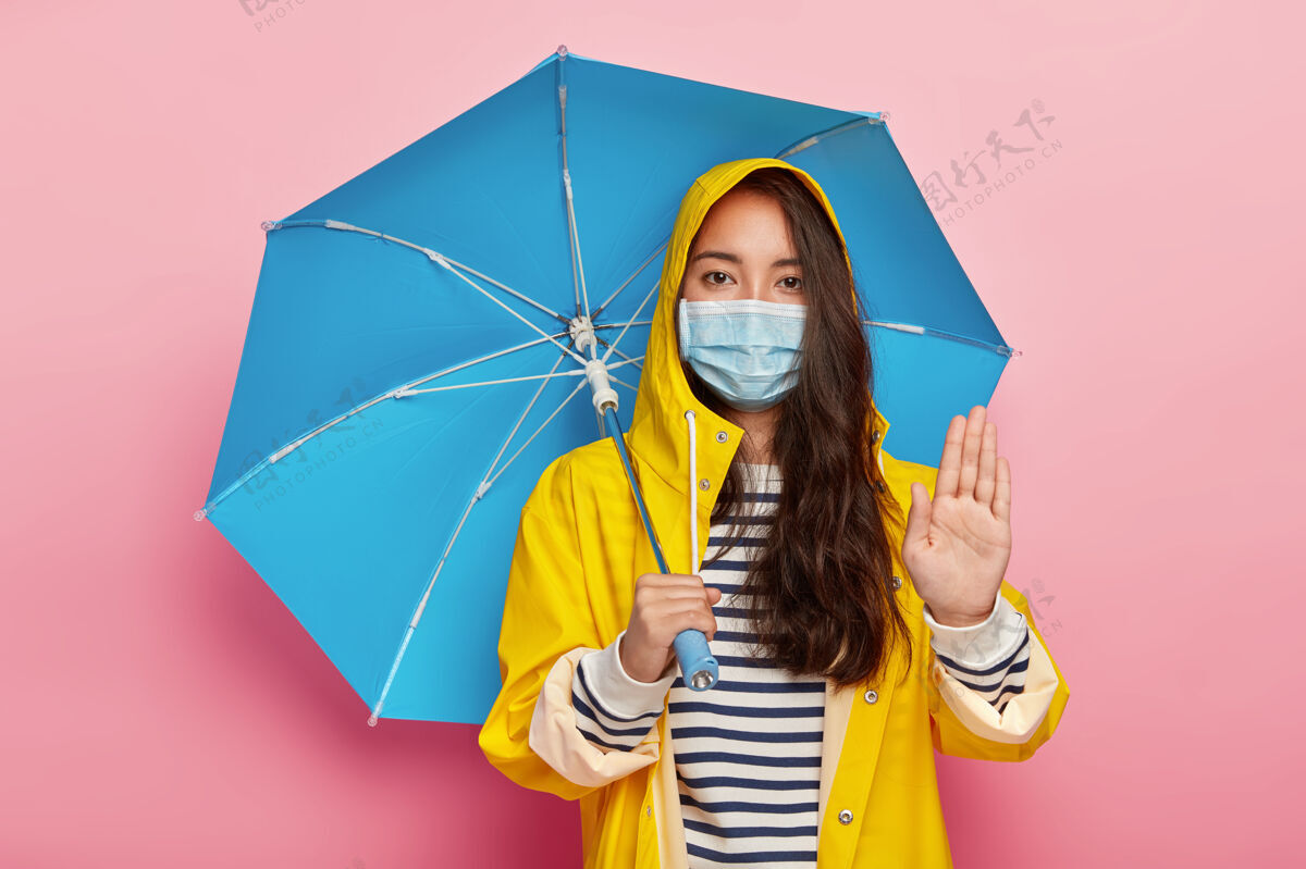 空气严肃的女孩做停车手势 要求不要污染环境 在酸雨中行走 戴防护面具减少呼吸污染物 穿雨衣 躲在雨伞下肖像护理女性