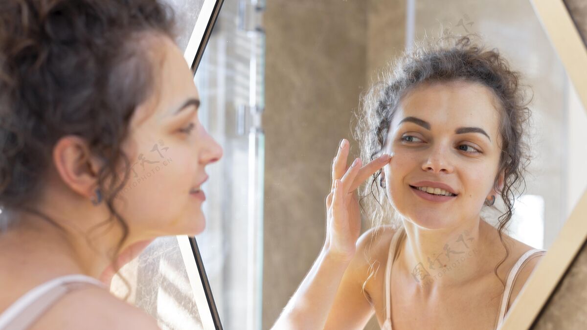 模特女人照镜子在脸上涂面霜美容自我护理女人