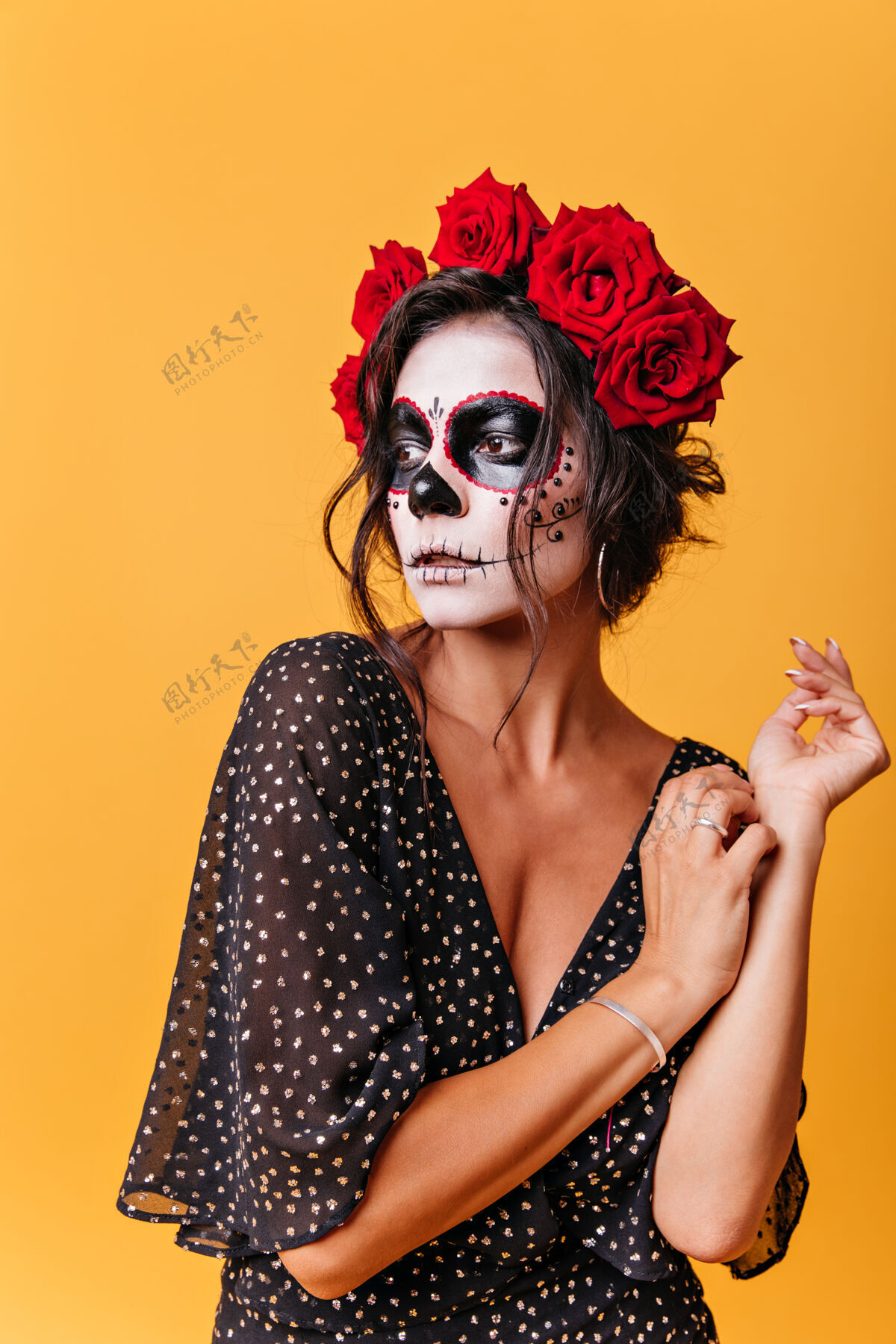 邪恶一幅卷曲的女人的肖像 头发上插着红色的大玫瑰 神秘地看着远处的橙色墙壁来自墨西哥的女孩模特 在万圣节化妆人物魔鬼肖像