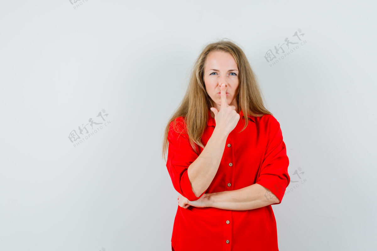 女性穿红衬衫的金发女郎用手指抚摸鼻子 看起来很可爱 时尚姿势华丽