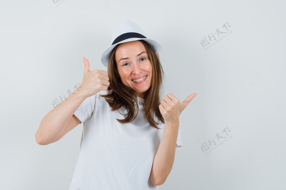 秀穿着白色t恤 戴着帽子的年轻女孩向上竖起了大拇指 看上去很开心 正前方的景色拇指微笑年轻