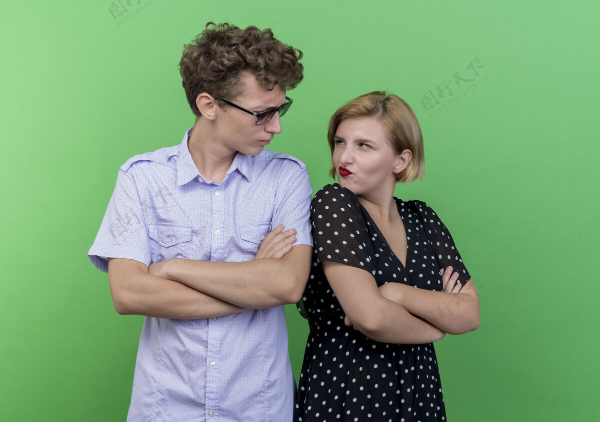 背年轻漂亮的夫妇男人和女人背靠背地站在一起看着对方皱着眉头越过绿色的墙皱眉年轻女人
