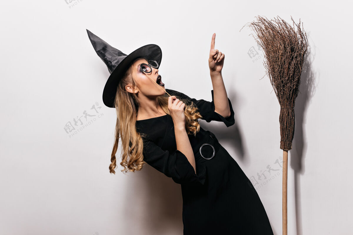女巫穿着万圣节服装的卷发女孩抬起头来戴着黑帽子的迷人女巫和老扫帚合影庆典化妆舞会魔术师