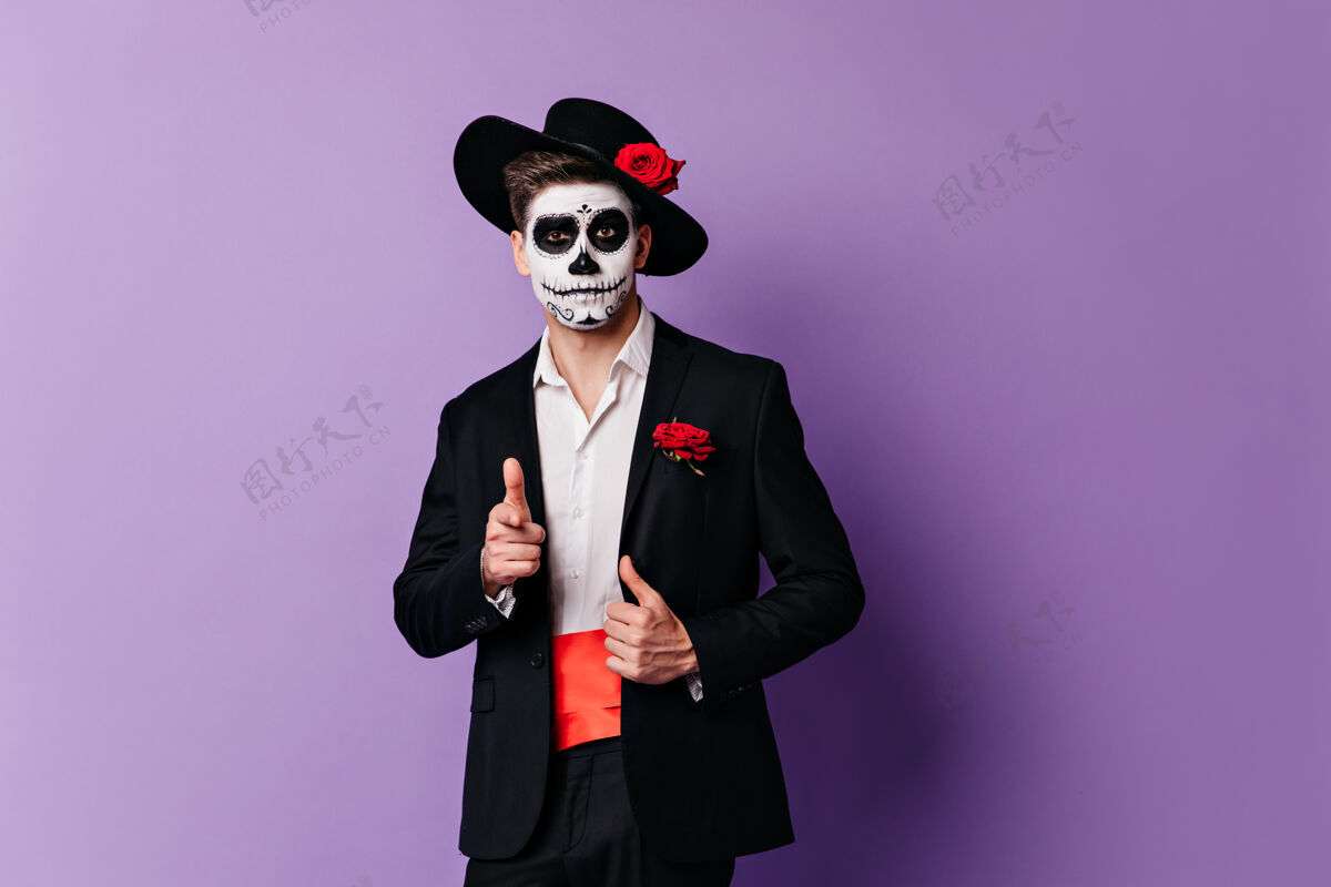 墨西哥戴着骷髅面具的滑稽家伙的特写肖像 对着镜头展示手指面部艺术死亡之日传统