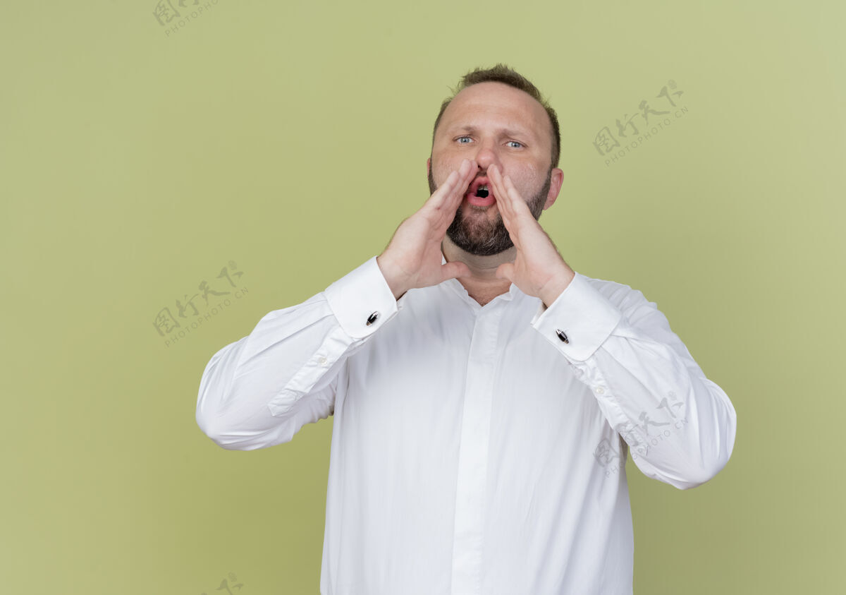 手一个留着胡子的男人穿着白衬衫 站在光墙上 用手靠近嘴巴喊着或叫着人喊站