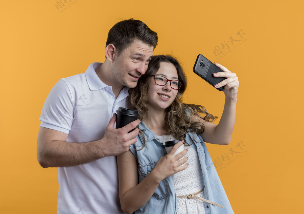 情侣一对穿着休闲服的年轻夫妇站在一起自拍 在爱中快乐 在橘色的墙上玩得开心乐趣男人休闲