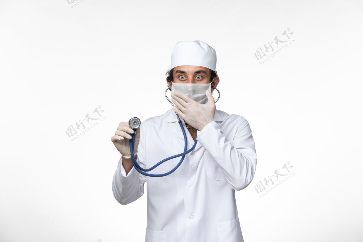 套装正面图：男医生穿着医疗服 戴着口罩以防病毒感染-使用听诊器对白色桌面病毒疾病进行病毒感染-大流行防护冠状病毒预防外套