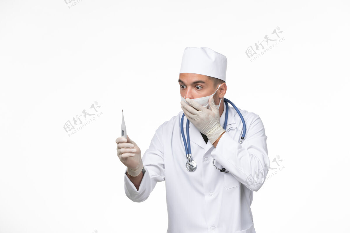 疾病正面图：男医生穿着防毒服 戴着防冠状病毒口罩 手持白墙病毒-疾病大流行病毒制服专业