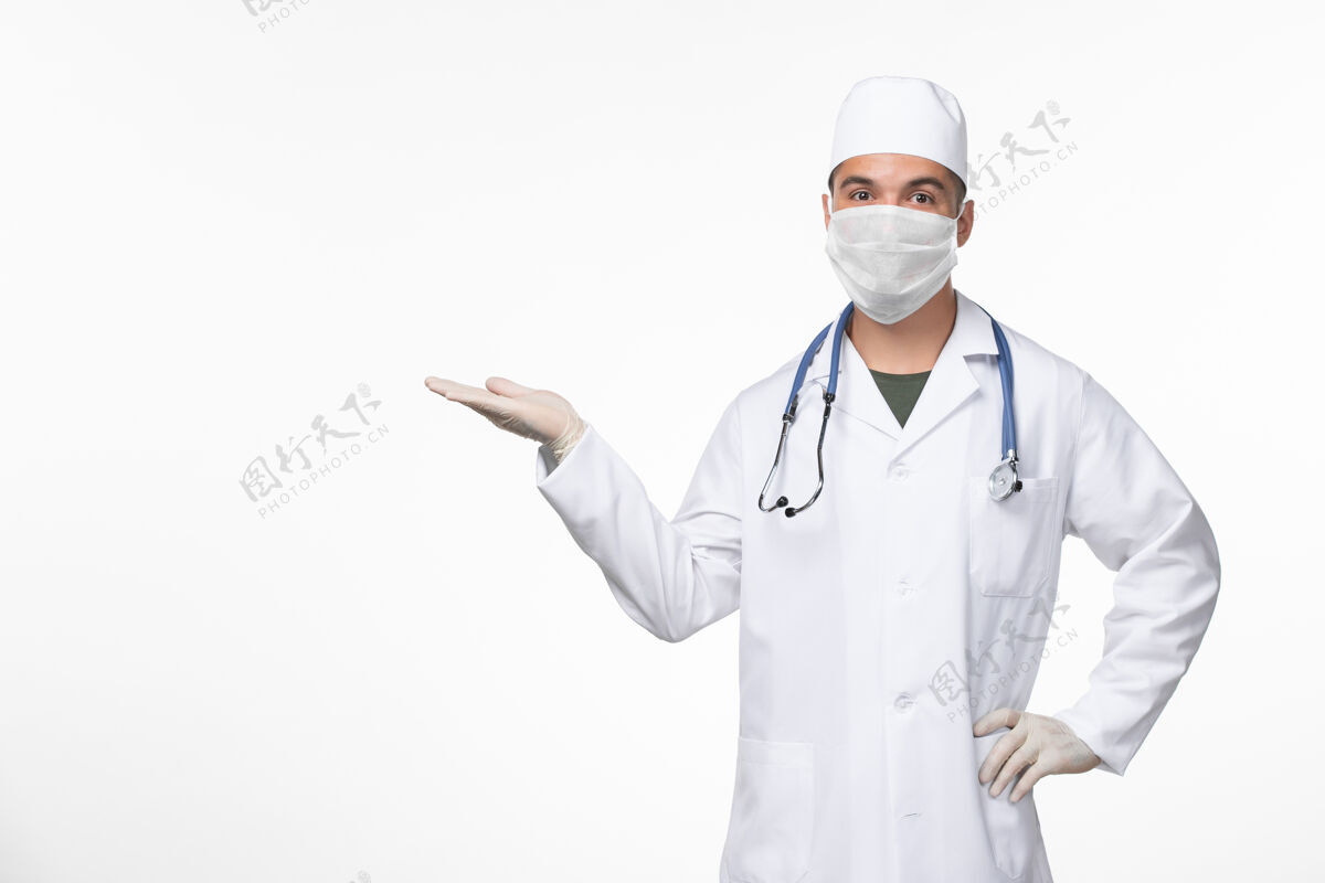 外套正面图：男医生穿着医疗服 戴着口罩 用听诊器对着白墙病毒-病毒-疾病大流行男性对抗听诊器