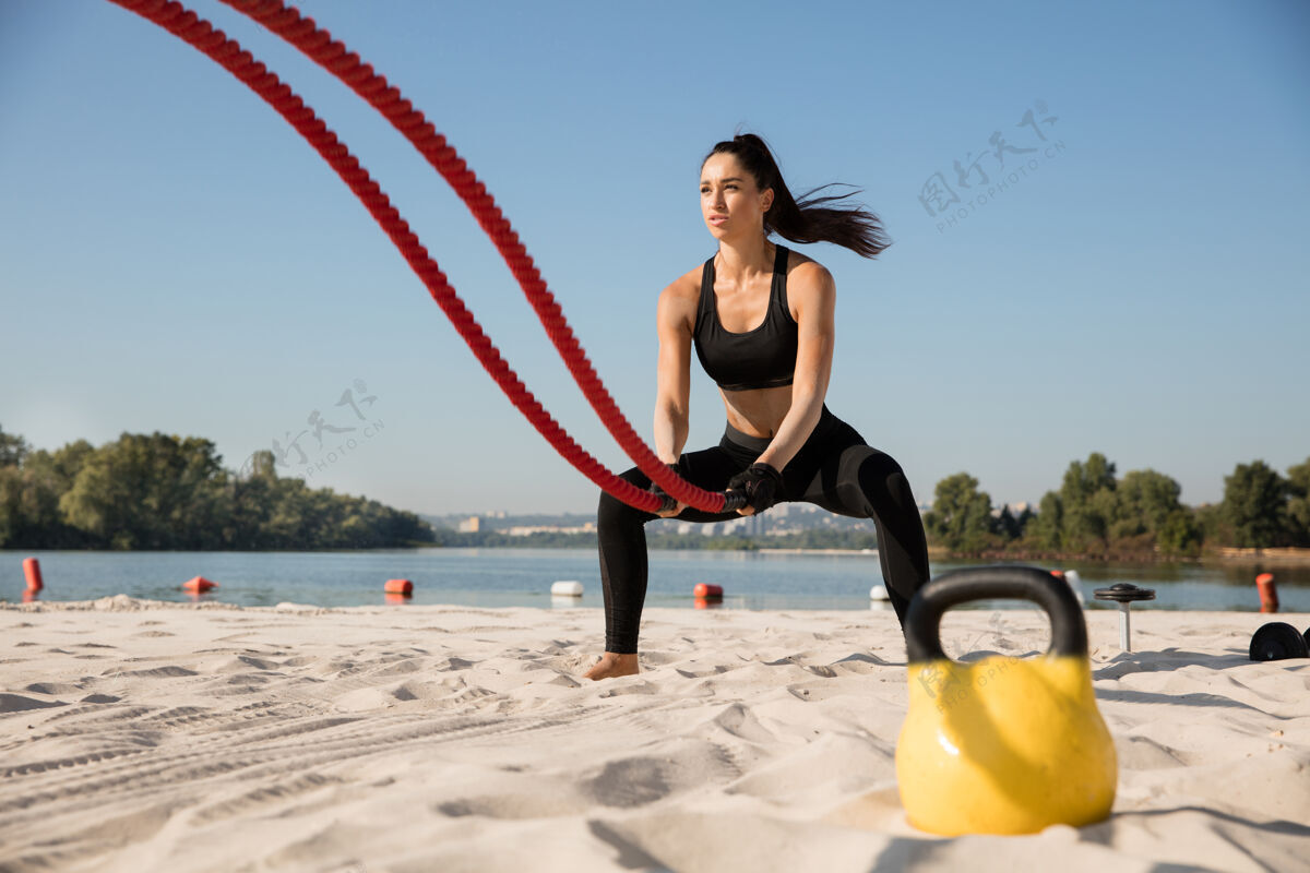 运动员年轻健康的女人在沙滩上用绳子锻炼身体河流力量练习
