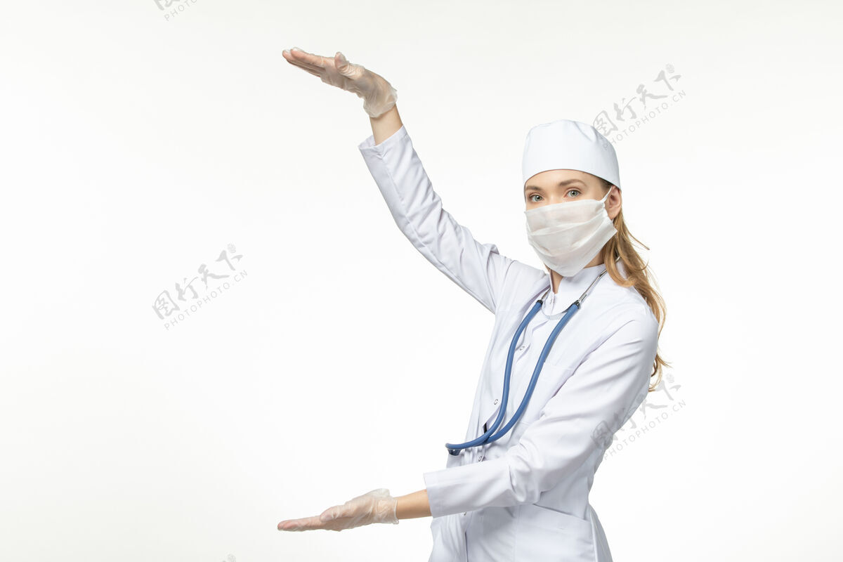 冠状病毒正面图：穿着白色医疗服 戴着口罩的女医生在白墙上抵御冠状病毒-大流行性疾病医生大流行套装