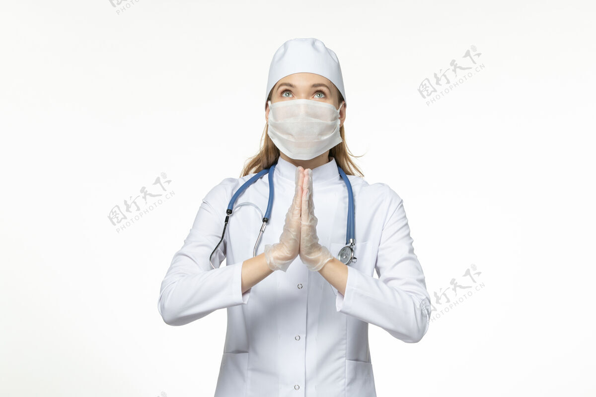 人员正面图女医生身穿医疗服戴口罩因冠状病毒祈祷台上有淡白色病毒病冠状病毒-大流行病毒病听诊器祈祷视图
