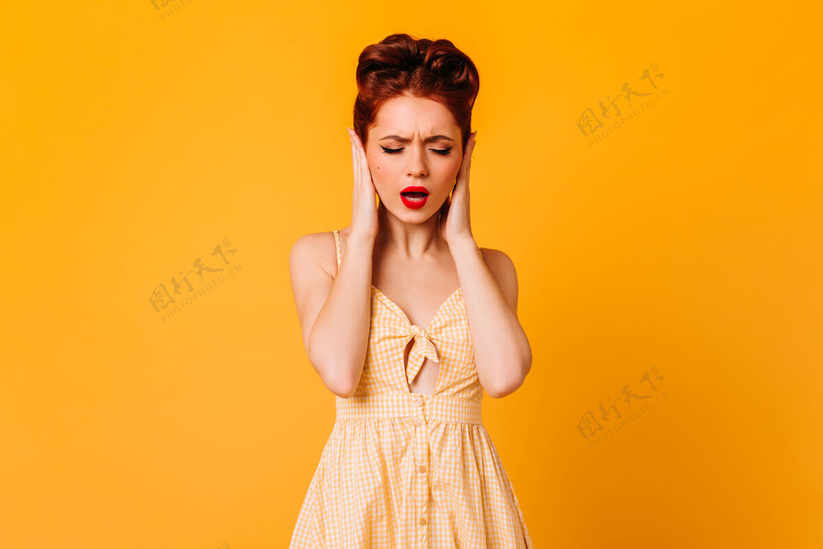 情感用手捂住耳朵的心烦意乱的女模特黄色空间里孤立的漂亮白人女人的摄影棚镜头姜无忧无虑服装