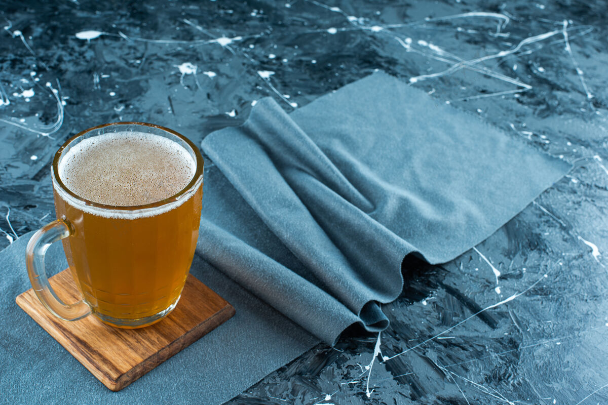 欢呼一杯啤酒放在蓝色的布料上泡泡啤酒厂开胃菜