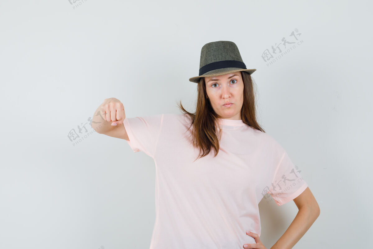 积极年轻女性穿着粉色t恤 戴着帽子 用拳头威胁 表情严肃正面视图帽子拳头肖像