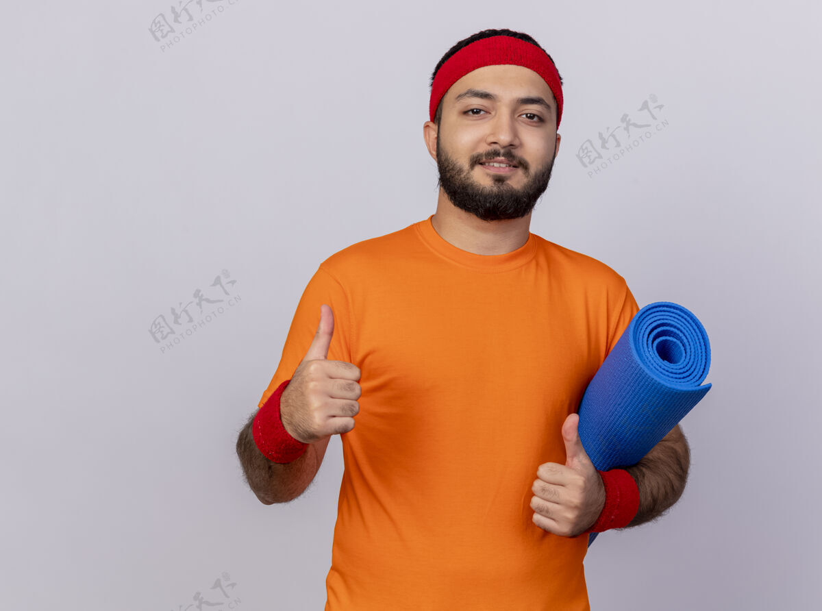 腕带高兴的年轻运动男子戴着头带和手环举行瑜伽垫运动垫子头带