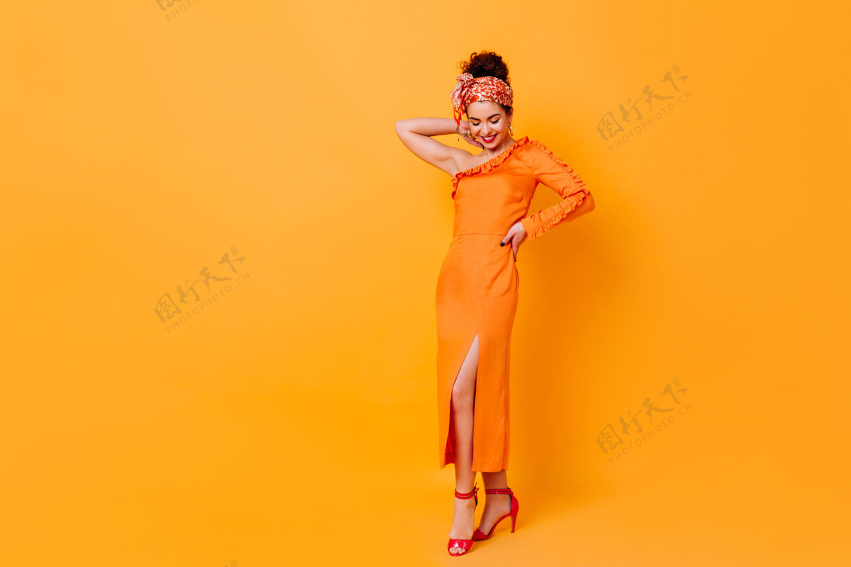 红唇身着丝绸长裙 头上有开叉和围巾的时尚女士在橙色空间摆姿势的全长照片蓝眼睛夏装橙色连衣裙
