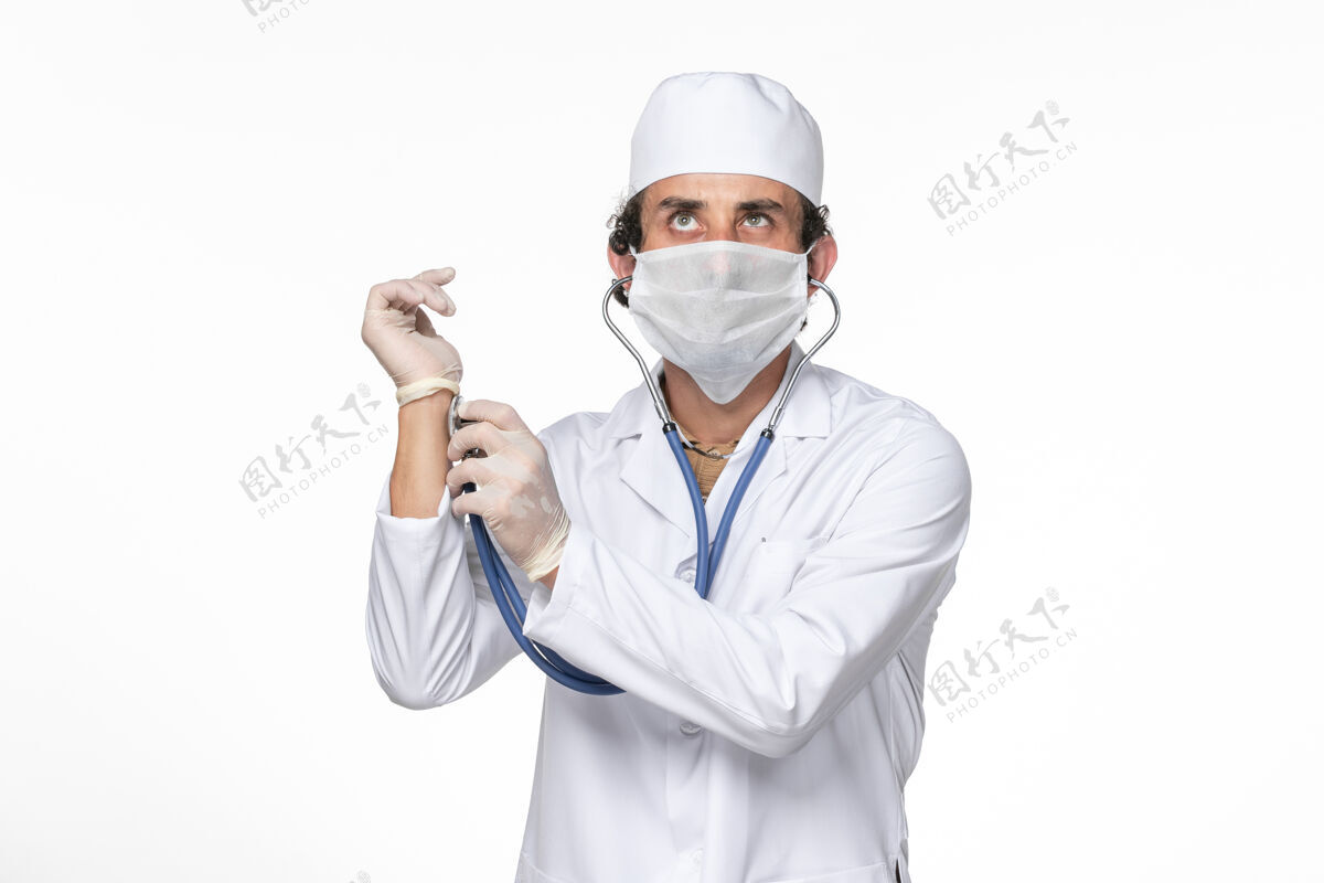 男人正面图：男医生穿着医疗服 戴着口罩以防感染冠状病毒-在白墙冠状病毒大流行药物上检查脉搏大流行医疗专业