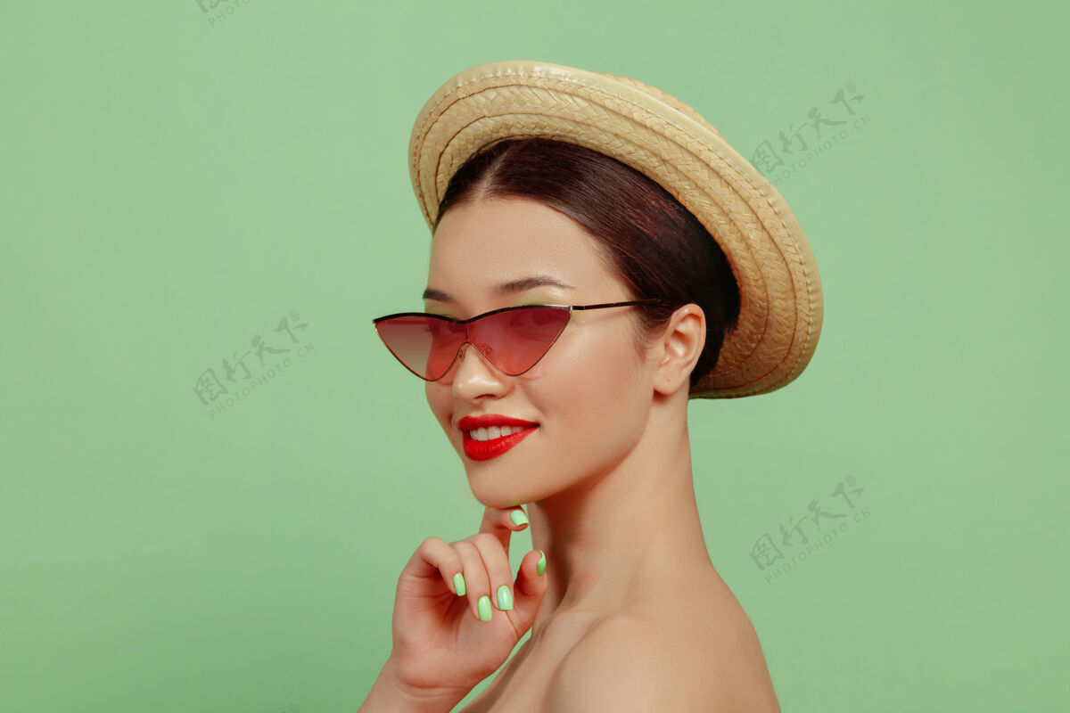 女人美丽女人的画像 明亮的妆容 红色的眼镜和帽子在绿色空间时尚和时尚的制作和发型夏天的颜色健康漂亮严肃