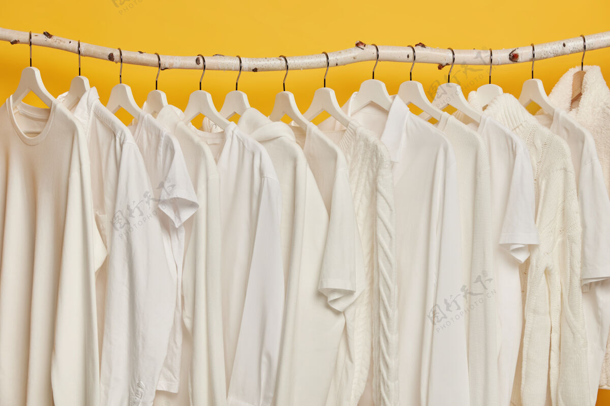 焦点同样的白色衣服放在壁橱的木架上衣架上的衣服收藏 隔离在黄色背景上零售商店白色