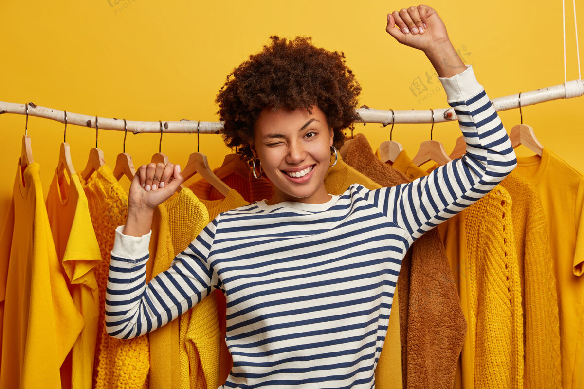 闪烁相当精力充沛的美国黑人妇女眨眼 跳舞 穿条纹套头衫 站在衣架上 买新衣服商店商业高兴