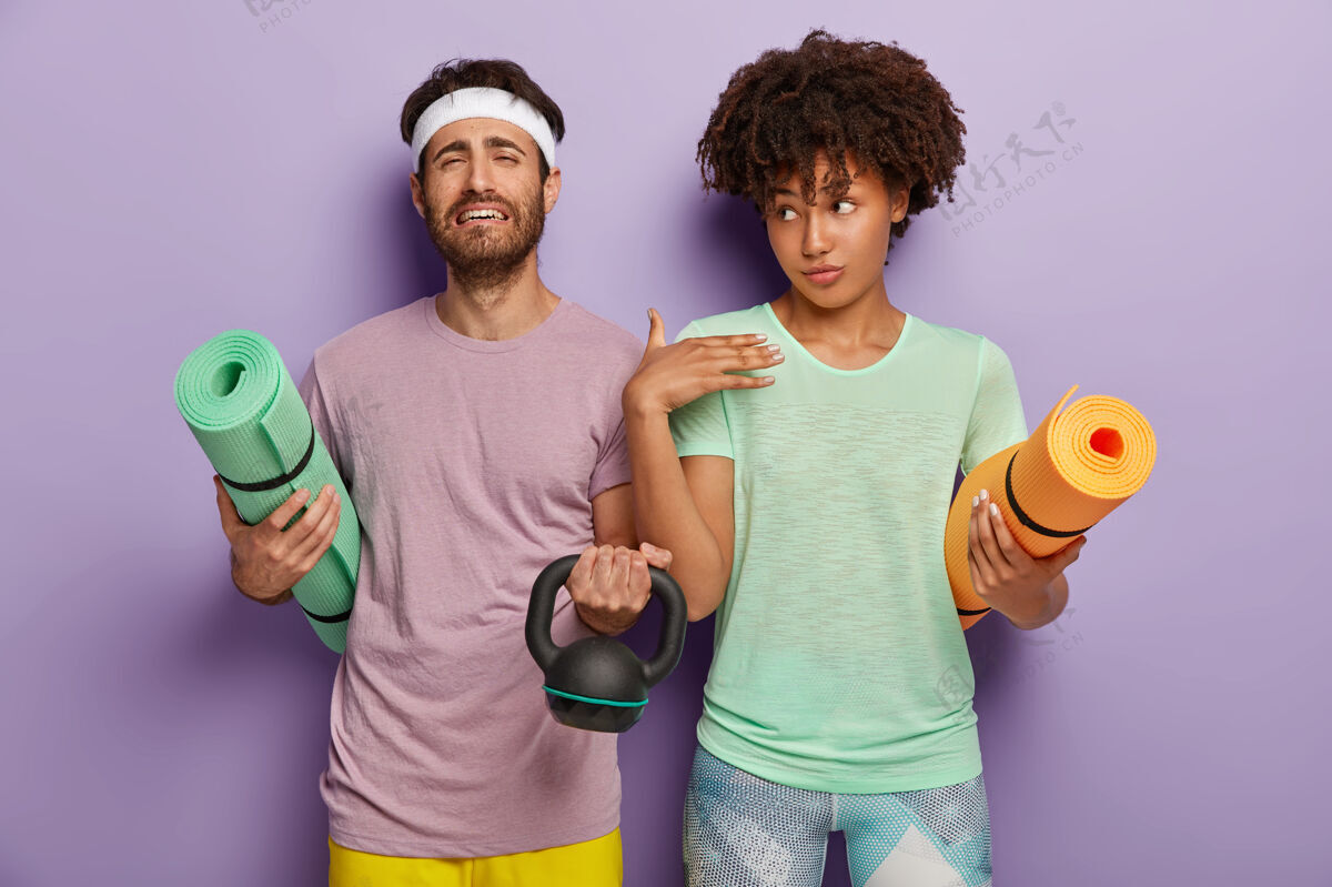运动员心烦意乱的没刮胡子的男人抱着卷起的卡雷马特 举重 参加运动 在紫色背景下站在一起 穿着t恤 进行健身训练人 运动 动力室内健身卷发