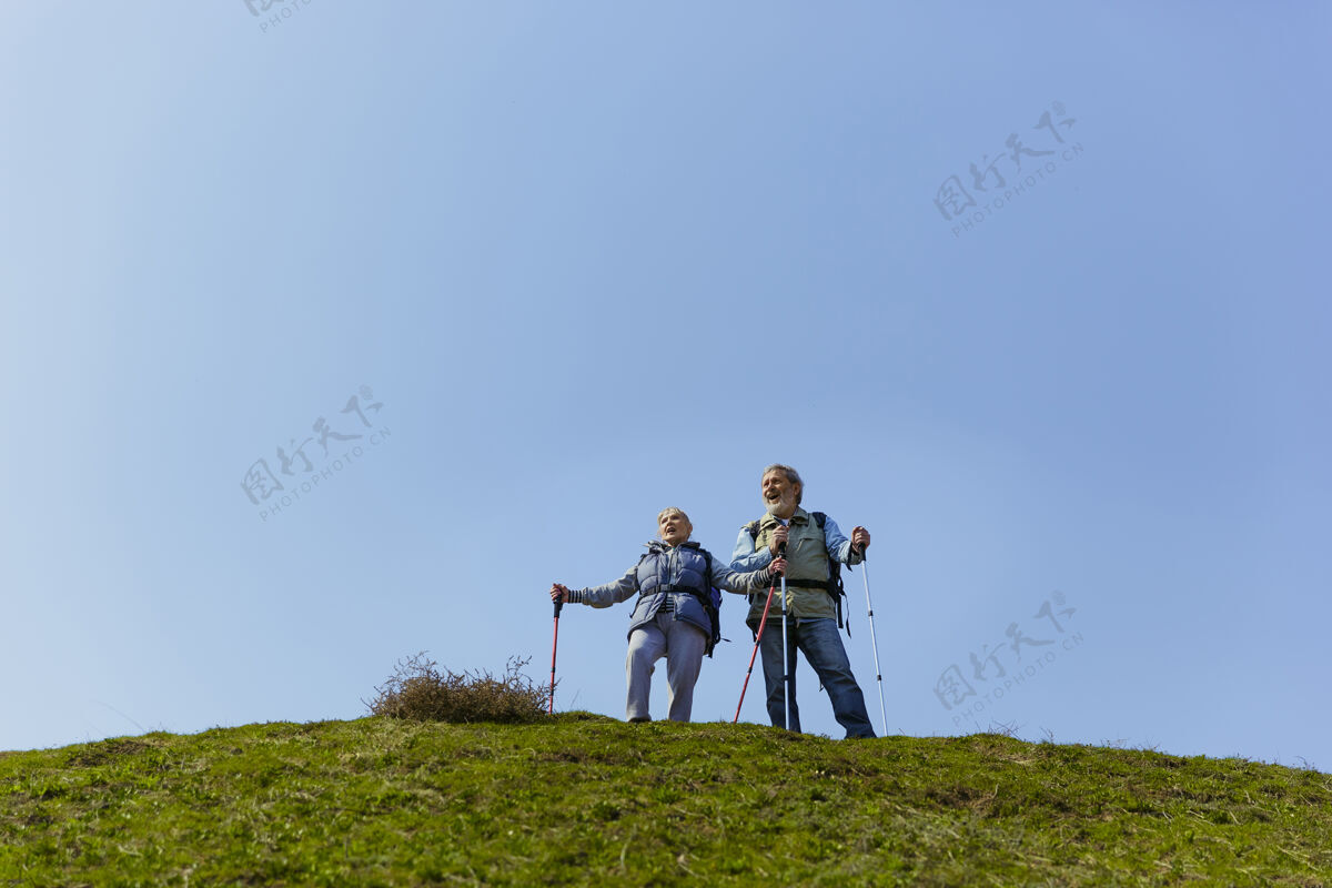 胡须在阳光明媚的日子里 一对穿着旅游服装的老人在绿油油的草坪旁散步活跃女人家庭