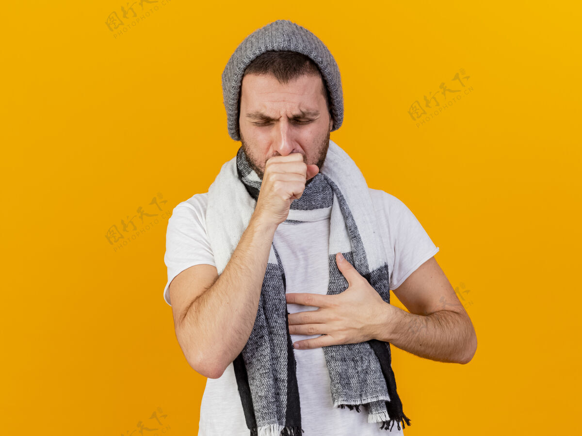 帽子咳嗽的年轻病人戴着冬天的帽子和围巾把手放在胸前隔离在黄色咳嗽冬天男人
