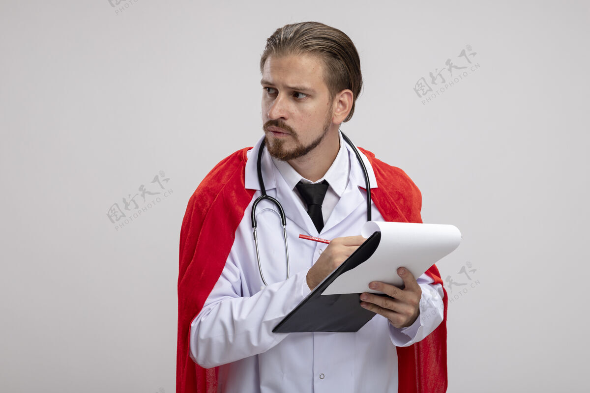 年轻年轻的超级英雄穿着医用长袍拿着听诊器拿着笔看着身边长袍壁板拿着