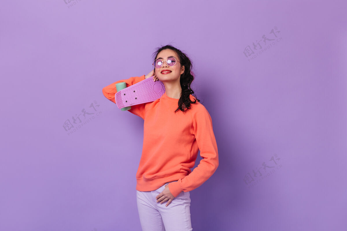 女性戴着眼镜拿着长板的亚洲女人摄影棚拍摄的日本女人在紫色背景上拿着滑板欢呼青少年情感