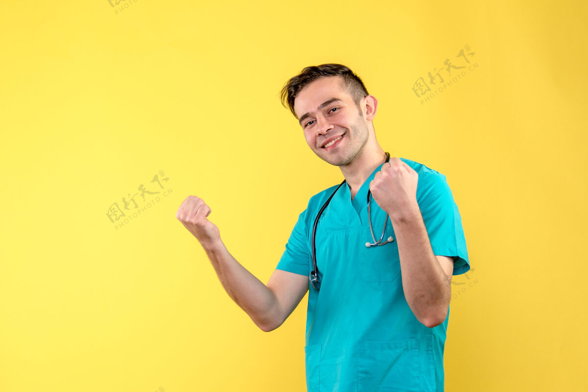 正面黄色墙上微笑的年轻男医生的正面图健康人人