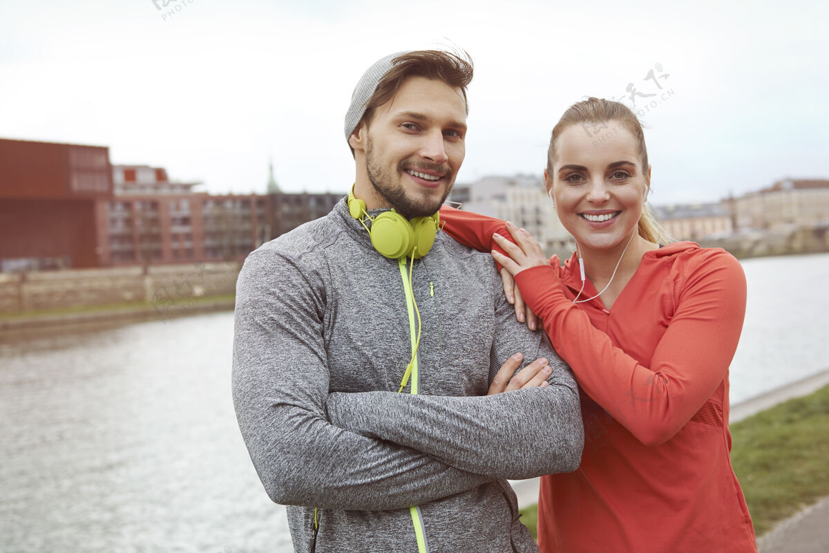 牙齿微笑快乐的运动情侣对着河摆姿势秋天体育训练站立
