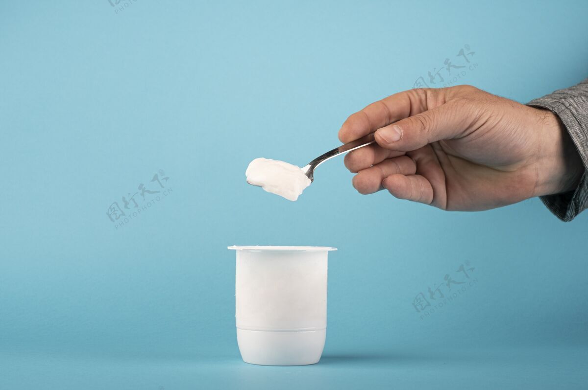 人特写镜头一个人拿着一个蓝色背景的白色酸奶勺子美味甜点餐