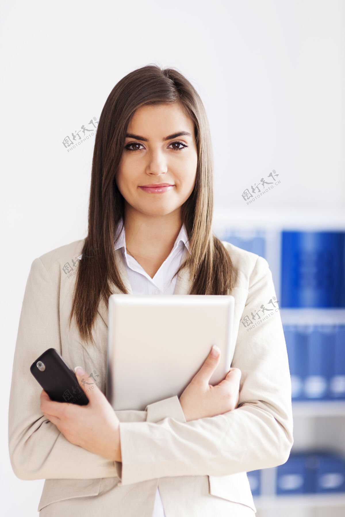 微笑手持数字平板电脑和手机的年轻女商人手持移动计算机设备