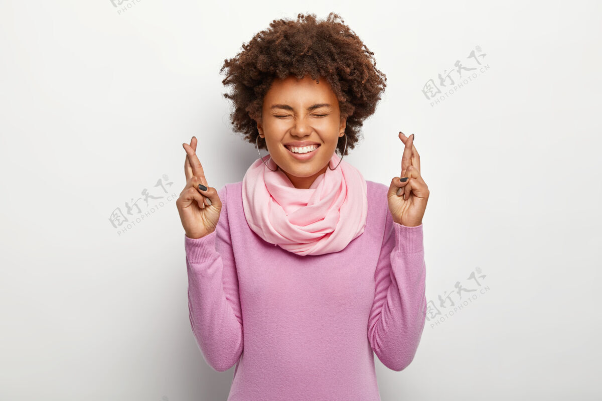 幸运充满希望的浓密卷发女人举起十指 专注于梦想 期待积极的结果 笑容灿烂 身穿紫色套装 靠着白色墙壁 祈求好运青年室内手势