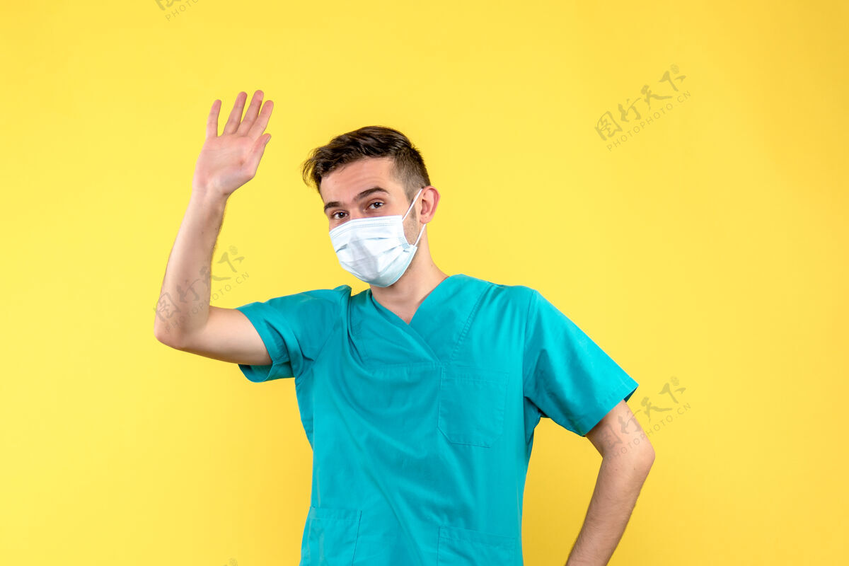 帅哥黄墙上戴着无菌口罩的男医生的正视图人人健康