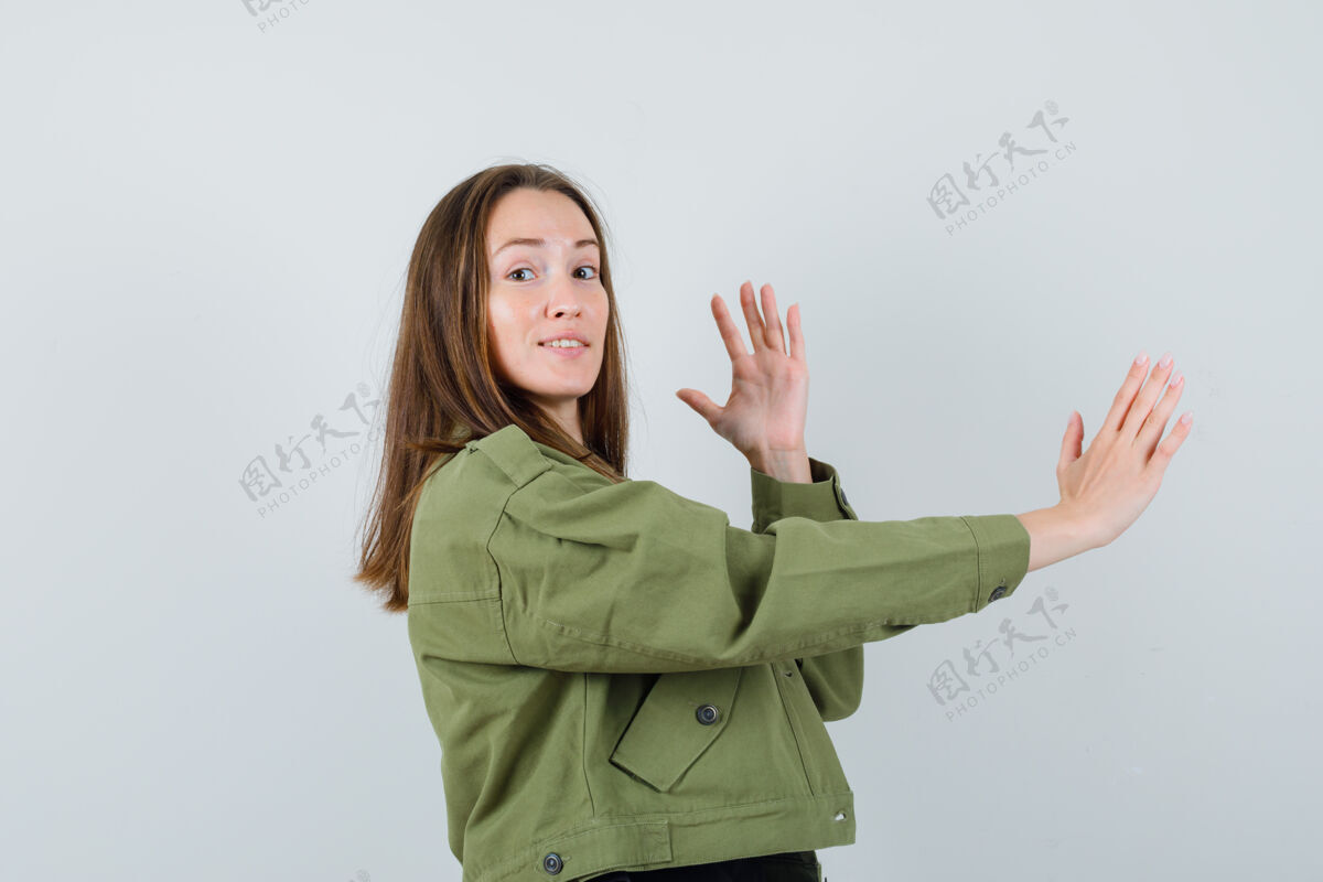 肖像穿着绿色夹克的年轻女子举起双手 手掌张开放在一边 小心地看着前方成人女人提高