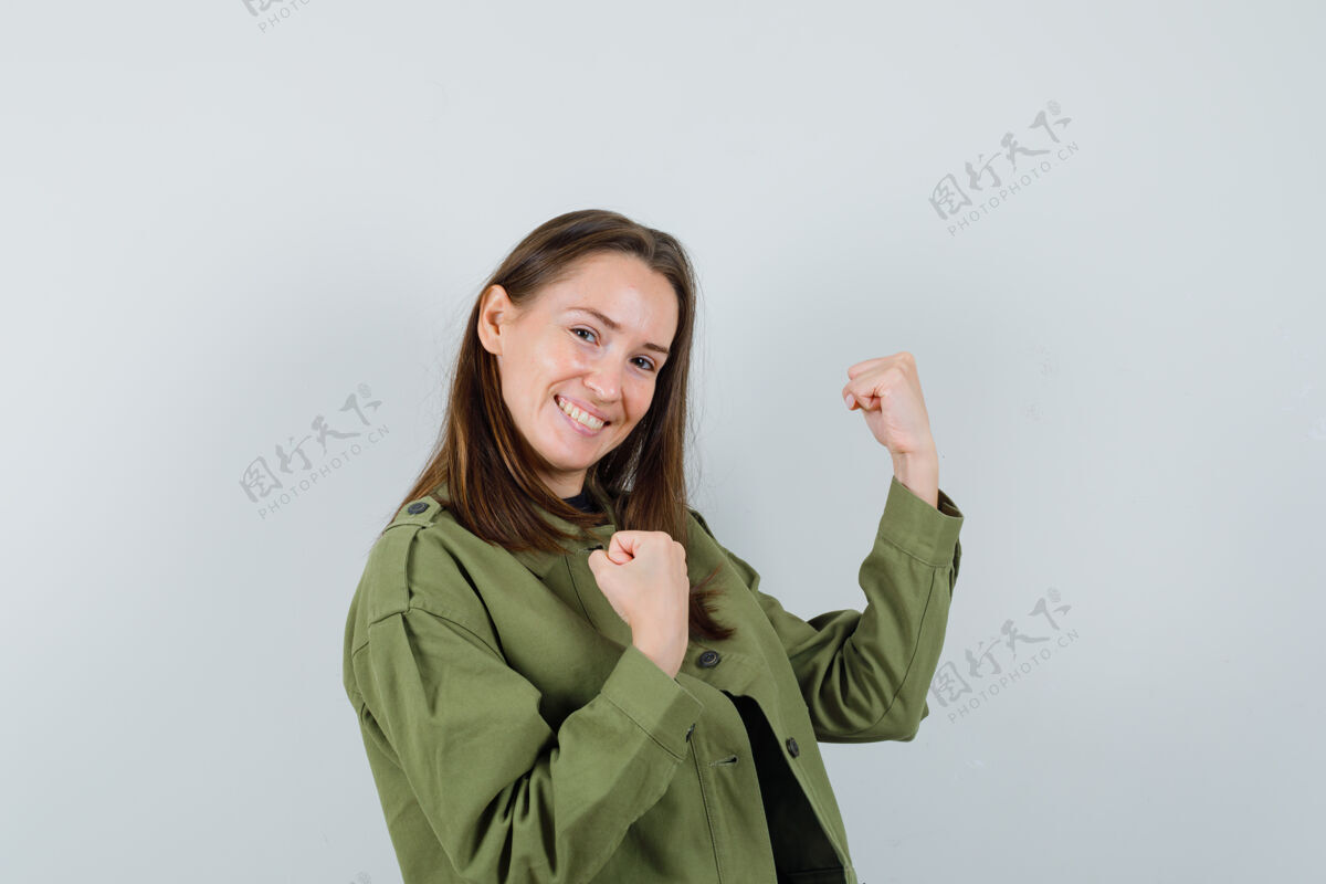 夹克身穿绿色夹克的年轻女子 展现出获胜者的姿态 看上去很欢快 正对着前方时尚微笑肖像