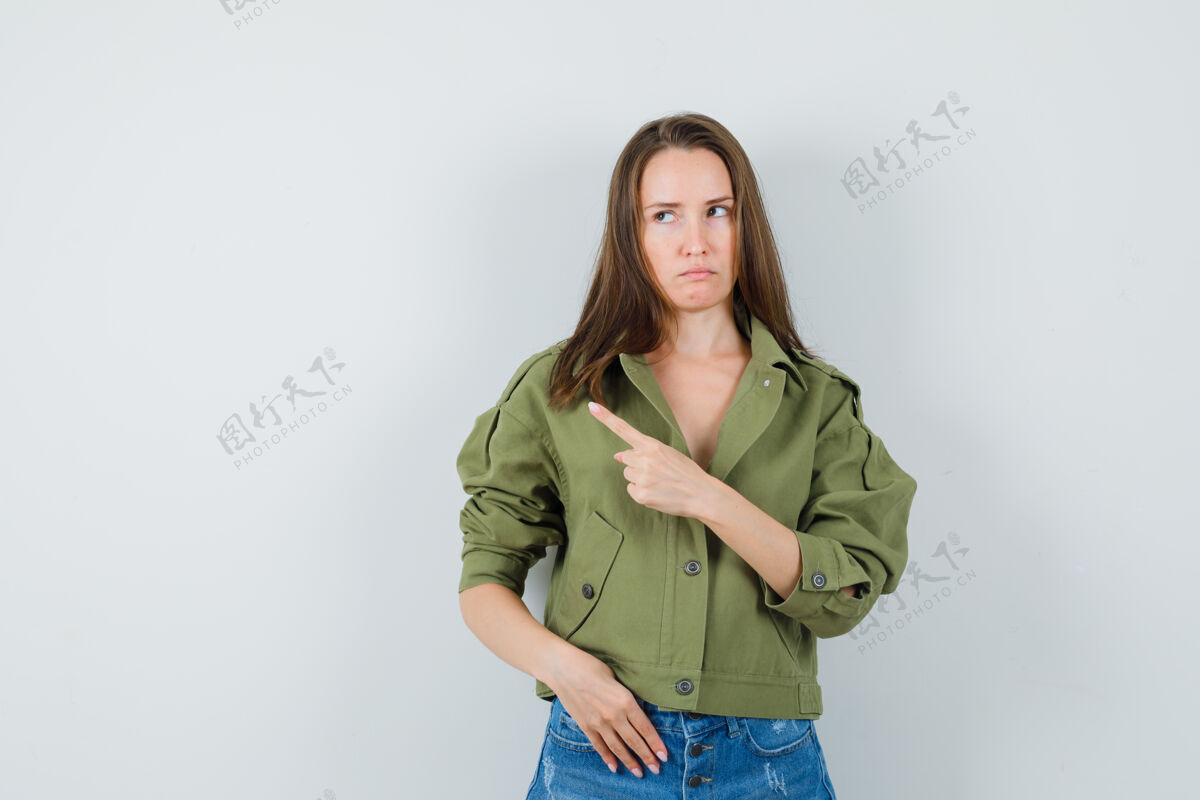 微笑年轻的女士指着左上角的夹克 短裤 看着不满前视图正面时尚礼服