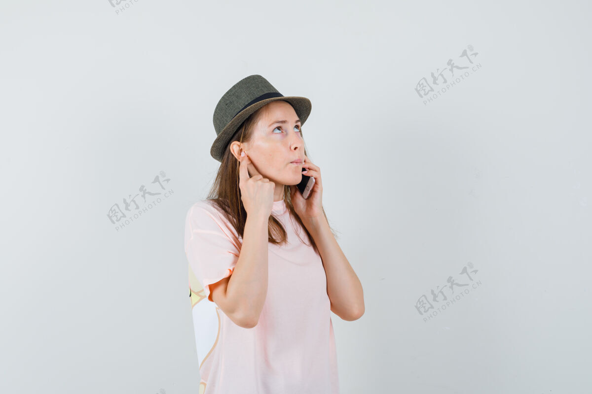 说话穿着粉色t恤 戴着帽子 面带沉思的年轻女孩在讲手机前视图童年小年轻