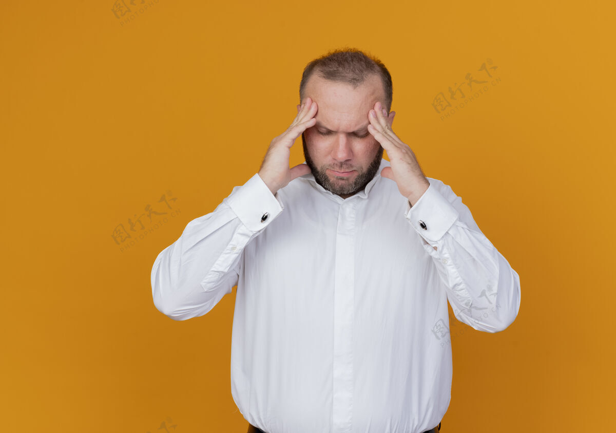 站一个留着胡子的男人 穿着白衬衫 站在橘色的墙上摸着太阳穴 头痛穿胡子摸