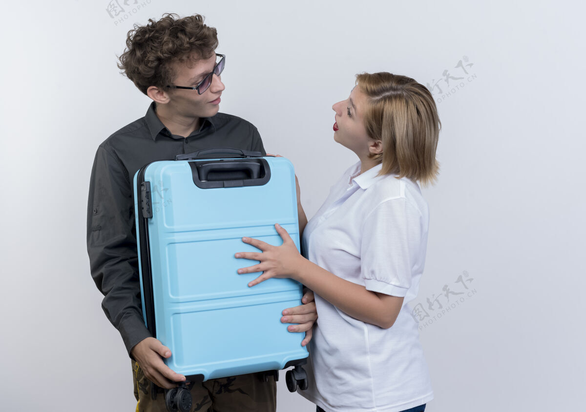 看着一对快乐的年轻游客 一男一女拿着手提箱 站在白色的墙壁上看着对方 惊讶不已抱着夫妇年轻人