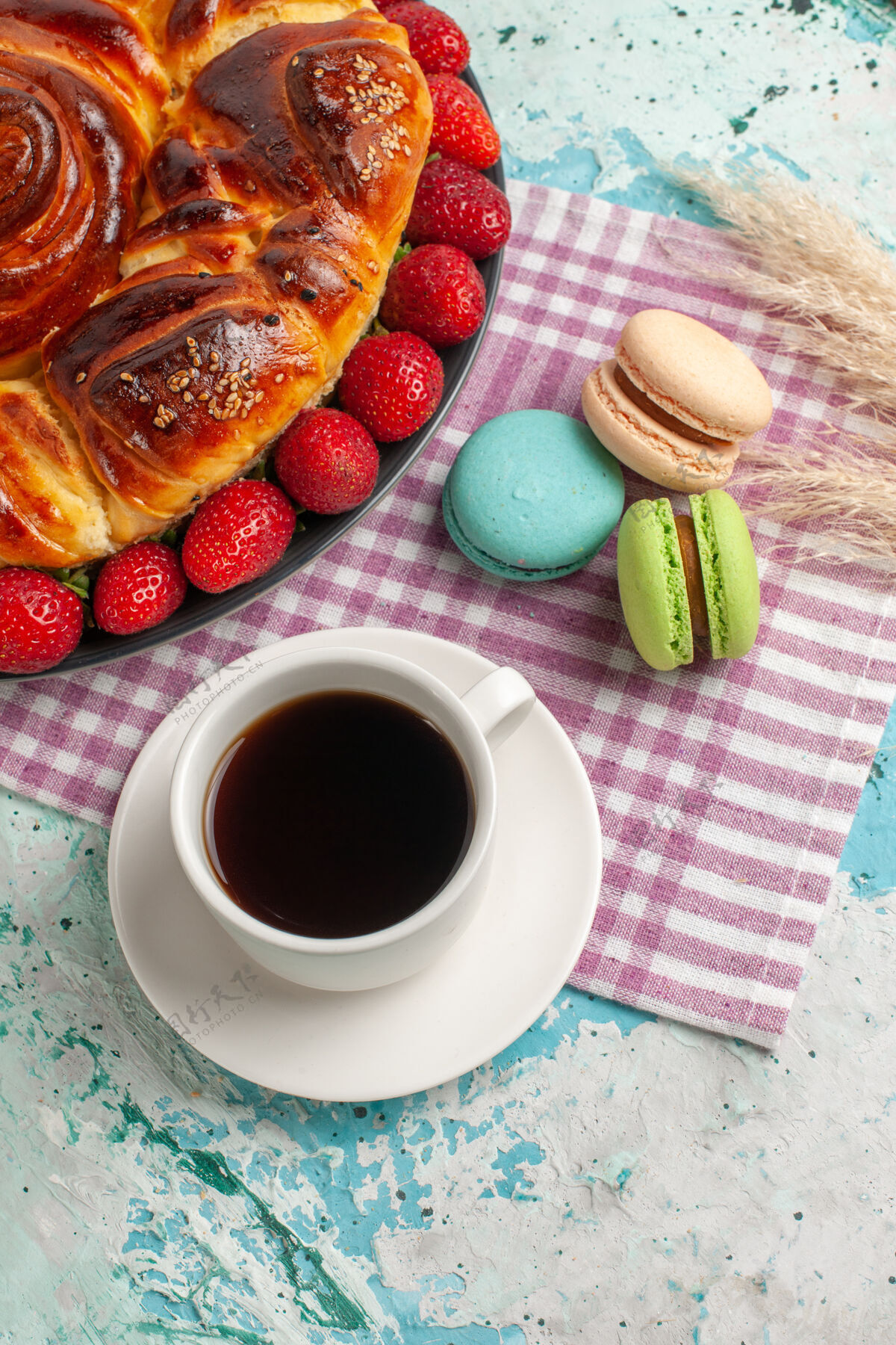 早餐俯瞰草莓派与法国马卡龙和茶在蓝色的表面生的饮料茶碟