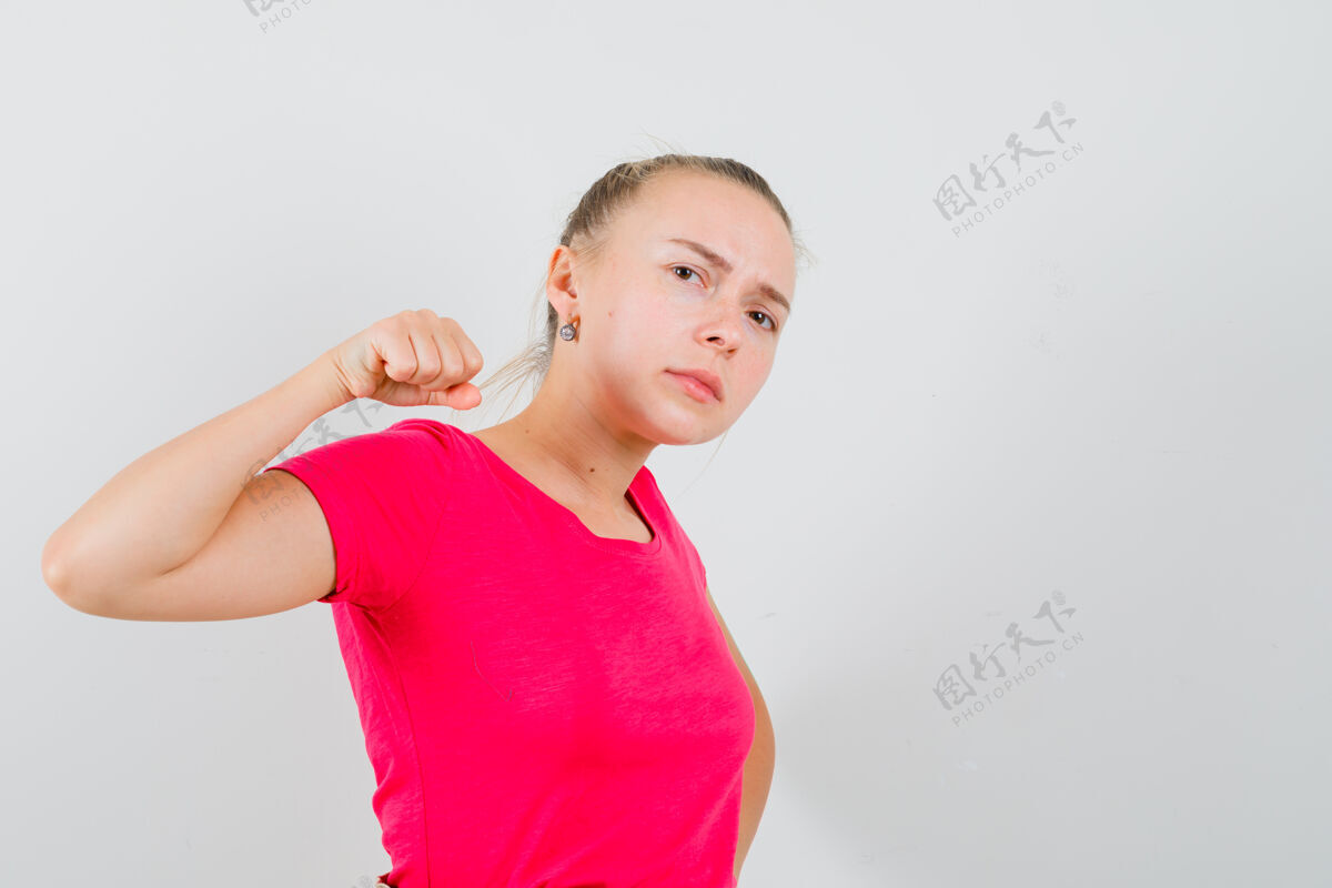 年轻一个穿着t恤衫的年轻女人用拳头威胁 看起来很恶毒模特快乐脸