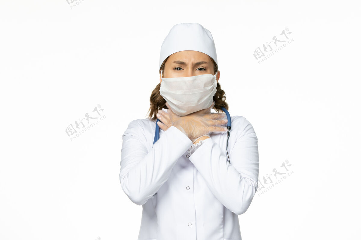 专业正面图年轻女医生戴着无菌口罩和手套 由于冠状病毒在浅白的表面大流行制服医生