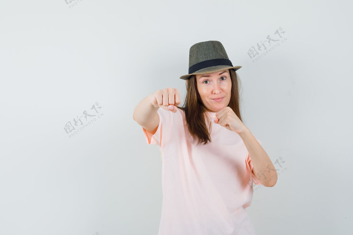 帽子年轻的女性站在战斗姿势在粉红色的t恤 帽子和看起来自信 前视图年轻姿势漂亮