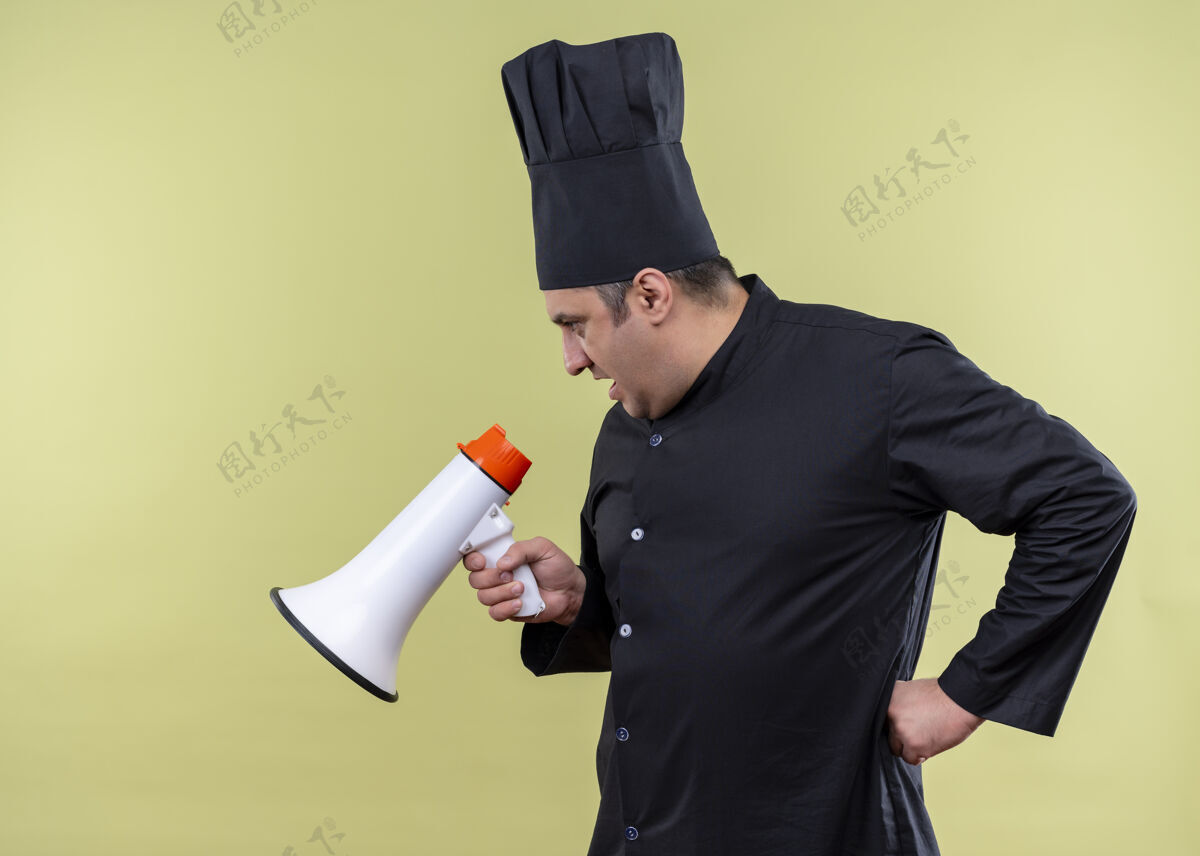 厨师男厨师身穿黑色制服 头戴厨师帽 站在绿色背景上对着扩音器大声喊叫扩音器穿站立