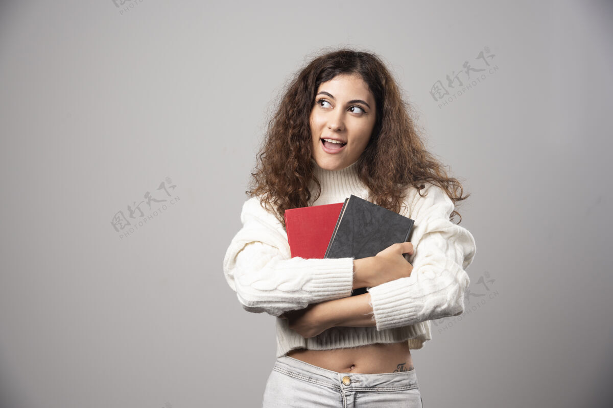 人在灰色的墙上拿着两本书的年轻女子高质量的照片微笑人女性